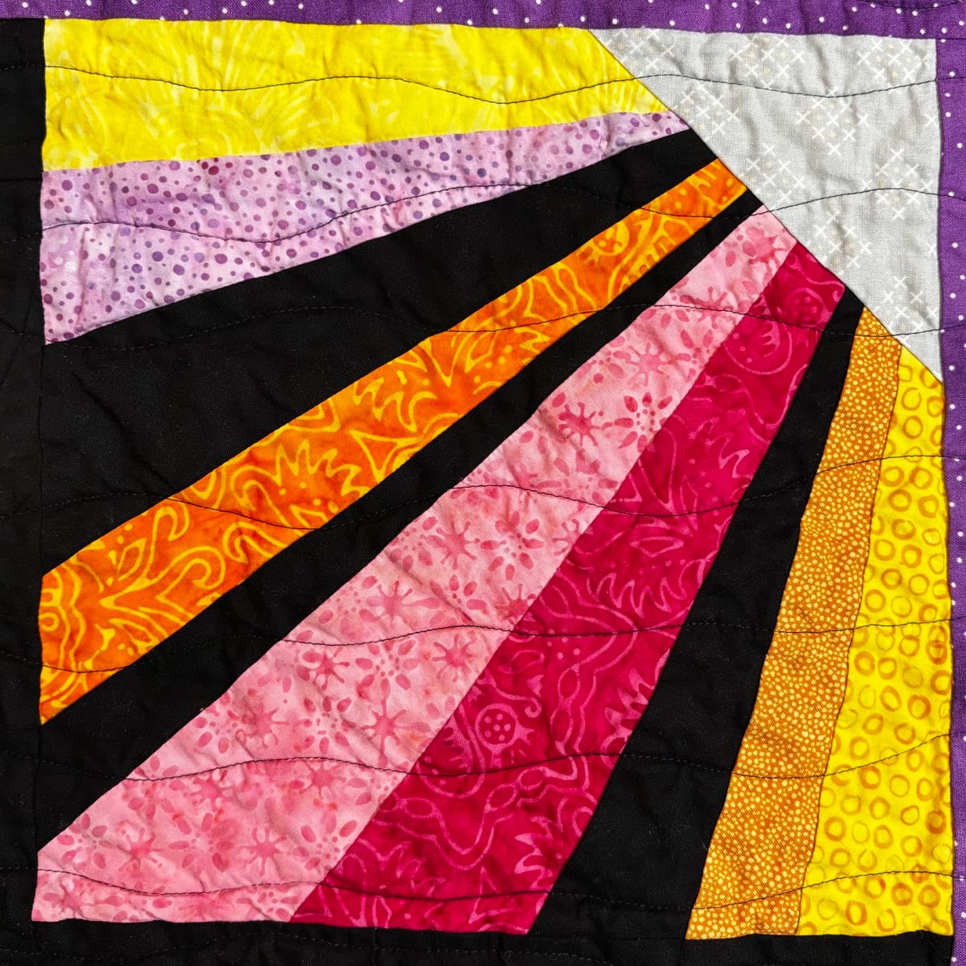 Quilted sunburst block with pink, orange, and yellow rays